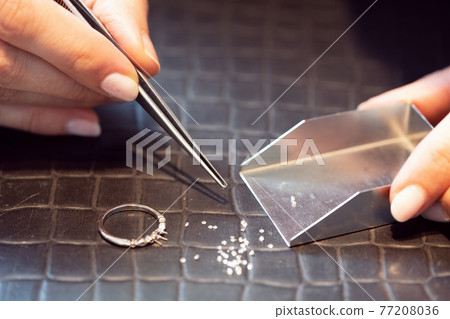 Jeweler sorting thru little diamonds in her workshop 77208036