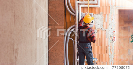 Male builder measuring the pipe attach on wall at construction site 77208075