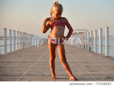 Child girl in a swimsuit stands on the pier at sunset Child girl in a swimsuit stands on the pier at sunset 77209093