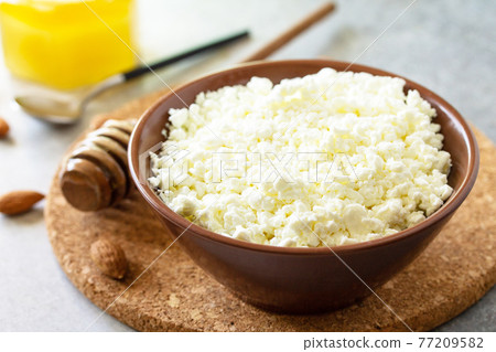 Rich in calcium healthy food. Tvorog, farmers cheese, curd cheese or cottage cheese in a bowl with honey and almond on stone table. Rich in calcium healthy food. Tvorog, farmers cheese, curd cheese or cottage cheese in a bowl with honey and almond on stone table. 77209582
