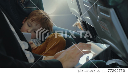 Boy using smart phone and father with tablet in plane Boy using smart phone and father with tablet in plane 77209750