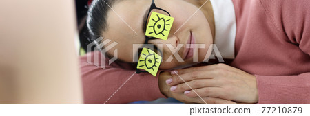 Tired woman lies at workplace with stickers on her eyes Tired woman lies at workplace with stickers on her eyes 77210879