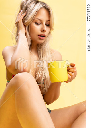 A girl sitting on the floor with her feet cross-legged keeps her head on a beautiful yellow background with a cup in hand yellow or pink and red fashion bikini beauty, pretty slim studio person A girl sitting on the floor with her feet cross-legged keeps her head on a beautiful yellow background with a cup in hand yellow or pink and red fashion bikini beauty, pretty slim studio person 77211710