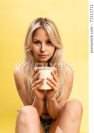 A girl sitting on the floor with her feet cross-legged keeps her head on a beautiful yellow background with a cup in hand yellow or pink and red playful bikini beauty, pretty beautiful model studio A girl sitting on the floor with her feet cross-legged keeps her head on a beautiful yellow background with a cup in hand yellow or pink and red playful bikini beauty, pretty beautiful model studio 77211711