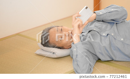 Senior man looking at a smartphone while lying down 77212461