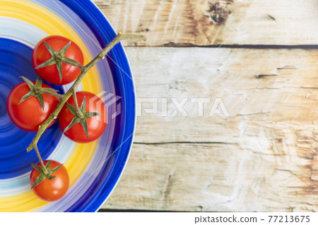 Cherry tomatoes on colorful striped plate and brown wooden background Cherry tomatoes on colorful striped plate and brown wooden background 77213675