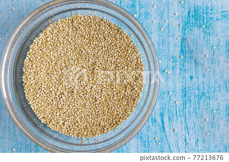 Raw quinoa grains inside transparent bowl, on blue table Raw quinoa grains inside transparent bowl, on blue table 77213676
