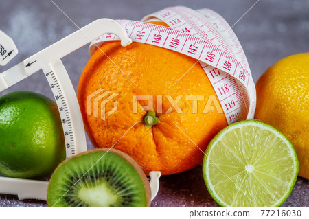An orange wrapped with a measuring tape and a caliper surrounded by fresh fruits An orange wrapped with a measuring tape and a caliper surrounded by fresh fruits 77216030