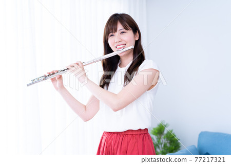 Woman playing the flute in the living room 77217321