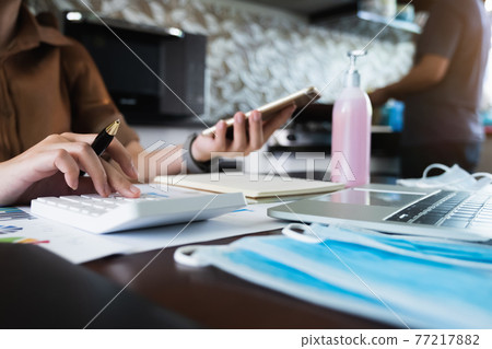 Close up Business woman using calculator and laptop for do math finance on wooden desk and cooking by her husband. work from home concept Close up Business woman using calculator and laptop for do math finance on wooden desk and cooking by her husband. work from home concept 77217882