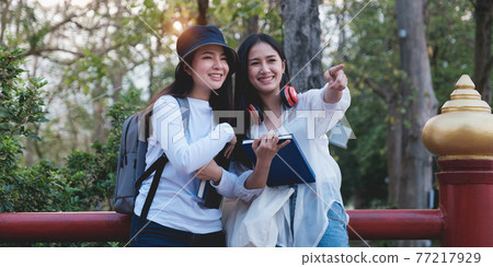 Two Young students from university enjoying excursion in park and pointing something when them interesting. Study, education, university, college, graduate concept. 77217929