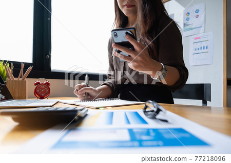 Young accountant marketing consultants and using calculator app by smartphone to analyze sales growth in the global workplace market. accounting concept 77218096