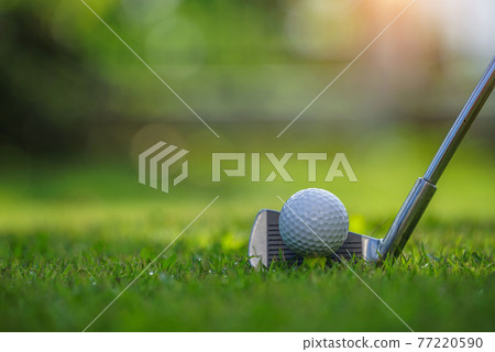 Closeup golf ball on tee ready to be shot. Golf ball on tee in the evening golf course with sunshine. Blurred set of golf clubs over green field background. 77220590