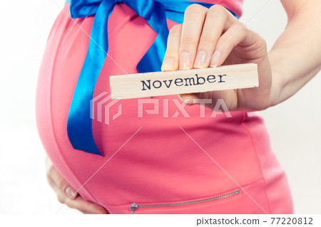Woman in pregnant wearing pink dress with blue ribbon and showing word november Woman in pregnant wearing pink dress with blue ribbon and showing word november 77220812