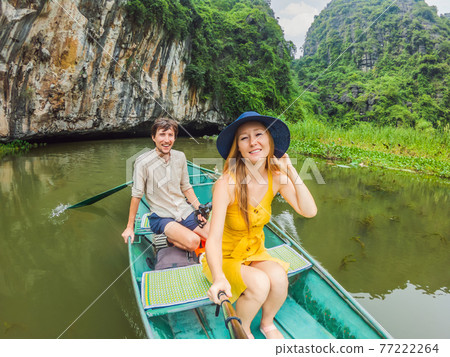 Happy family tourists in boat on the lake Tam Coc, Ninh Binh, Viet nam. It's is UNESCO World Heritage Site, renowned for its boat cave tours. It's Halong Bay on land of Vietnam. Vietnam reopens 77222264