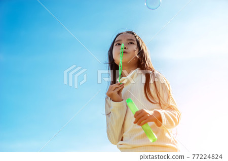 Portrait of funny lovely little Asian girl blowing soap bubbles in the park. Portrait of funny lovely little Asian girl blowing soap bubbles in the park. 77224824