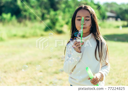 Portrait of funny lovely little Asian girl blowing soap bubbles in the park. Portrait of funny lovely little Asian girl blowing soap bubbles in the park. 77224825