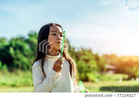Portrait of funny lovely little Asian girl blowing soap bubbles in the park. Portrait of funny lovely little Asian girl blowing soap bubbles in the park. 77224827