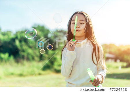 Portrait of funny lovely little Asian girl blowing soap bubbles in the park. Portrait of funny lovely little Asian girl blowing soap bubbles in the park. 77224828