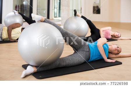 Sporty women and men doing exercises with pilates balls Sporty women and men doing exercises with pilates balls 77226598