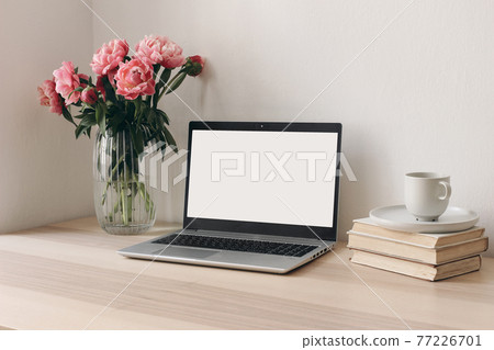 Notebook mock-up still life scene. Glass vase with pink peonies bouquet, books and cup of coffee on wooden table. Elegant feminine working space, home office concept. Living room interior design. Notebook mock-up still life scene. Glass vase with pink peonies bouquet, books and cup of coffee on wooden table. Elegant feminine working space, home office concept. Living room interior design. 77226701