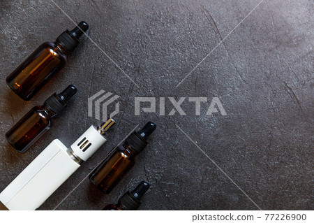 Vaping device e-cigarette electronic cigarette and liquid bottles on dark black stone shale background. Vape device for alternative smoking. Vaping shop concept. Gadget for vaper. Vaping accessories. 77226900