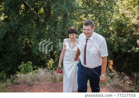 Newlyweds hold hands on the background of the forest Newlyweds hold hands on the background of the forest 77227558