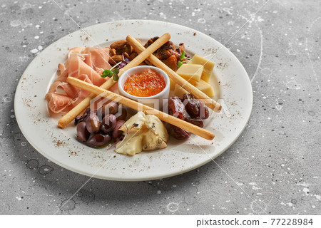 Set of snacks for wine. Prosciutto, parmesan, gorgonzola, almonds, olives, bread chips, mostard fruit confiture on gray marble background Set of snacks for wine. Prosciutto, parmesan, gorgonzola, almonds, olives, bread chips, mostard fruit confiture on gray marble background 77228984