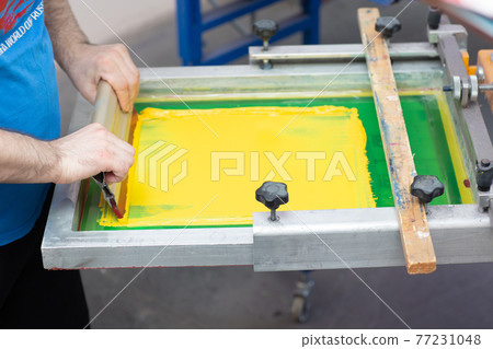 Serigraphy silk screen print process at clothes factory. Frame, squeegee and plastisol color paints Serigraphy silk screen print process at clothes factory. Frame, squeegee and plastisol color paints 77231048