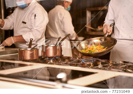 Cook frying vegetables on a pan in kitchen 77231049