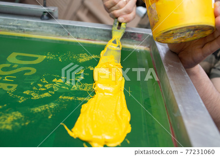 Serigraphy silk screen print process at clothes factory. Paint application to frame, squeegee and plastisol color paints Serigraphy silk screen print process at clothes factory. Paint application to frame, squeegee and plastisol color paints 77231060