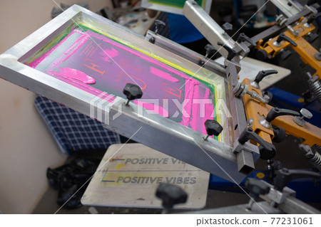Serigraphy silk screen print process at clothes factory. Frame, squeegee and plastisol color paints Serigraphy silk screen print process at clothes factory. Frame, squeegee and plastisol color paints 77231061