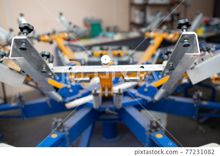 Serigraphy silk screen print process at clothes factory. Carousel Frame, squeegee and plastisol color paints Serigraphy silk screen print process at clothes factory. Carousel Frame, squeegee and plastisol color paints 77231082