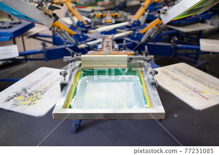Serigraphy silk screen print process at clothes factory. Carousel Frame, squeegee and plastisol color paints Serigraphy silk screen print process at clothes factory. Carousel Frame, squeegee and plastisol color paints 77231085
