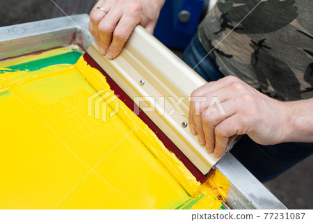 Serigraphy silk screen print process at clothes factory. Frame, squeegee and plastisol color paints Serigraphy silk screen print process at clothes factory. Frame, squeegee and plastisol color paints 77231087
