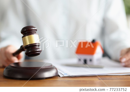 Judge holding wooden hammer near toy little house closeup 77233752