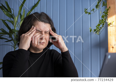 Middle-aged woman with a headache sitting in home and feel ill unhappy. 77234429