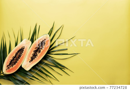 Fresh tropical papaya fruit halves on the palm leaf on a yellow background 77234728