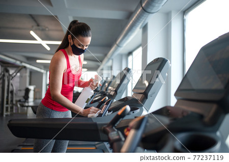 Fitness instructor with face mask disinfecting equipment in gym, coronavirus concept. 77237119