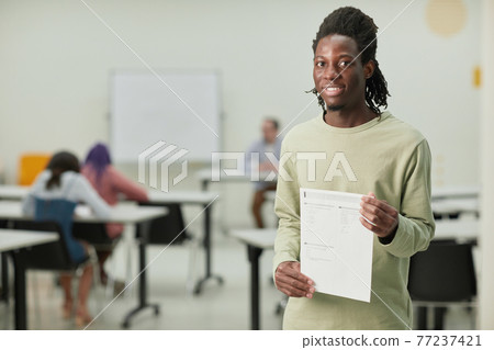 Young man holding test certificate in school Young man holding test certificate in school 77237421