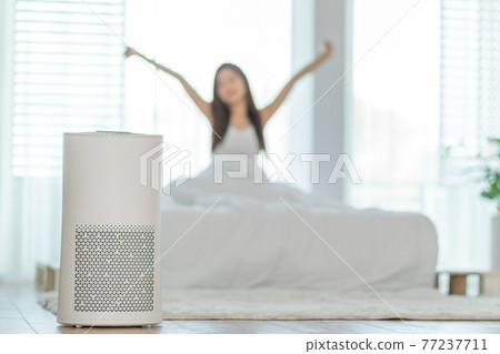 Wellness healthy woman wake up with Air purifier in cozy white bedroom for filter and cleaning removing dust PM2.5 HEPA in home,for fresh air and healthy life,Air Pollution Concept 77237711