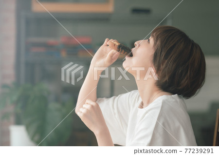 在客廳吃甜甜圈的年輕女人 77239291