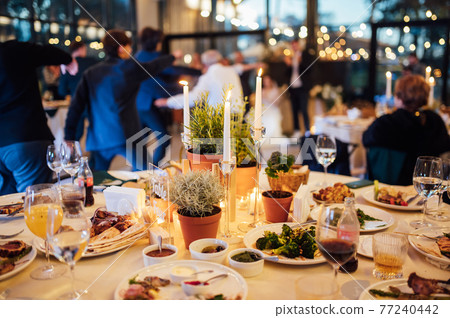 Flower and candle decoration for a wedding against the background of dancing guests Flower and candle decoration for a wedding against the background of dancing guests 77240442