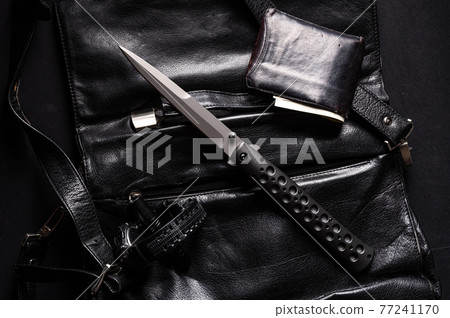 A large sharp knife and a purse of money. Knife on a leather briefcase. Clock and lantern. Black items on black. 77241170