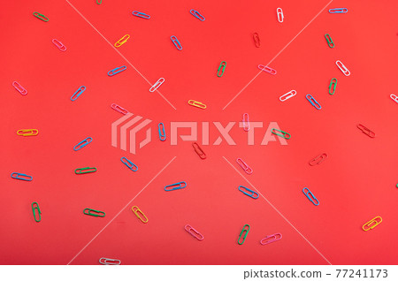 Various paper clips on the red table. Scattered paper clips. 77241173