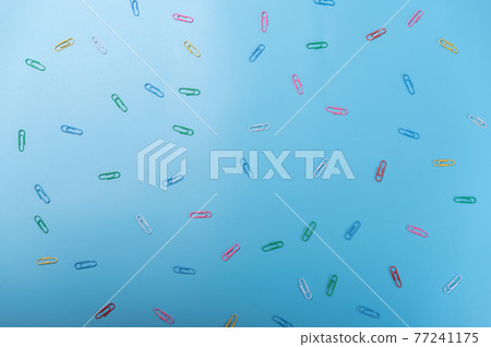 Multicolored paper clips on a blue background. Scattered paper clip on the table. 77241175