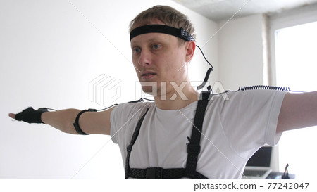 athletic man with beard wears motion capture suit with sensors headset moving in virtual reality taking something and looking at his hands excited experience cyber space online athletic man with beard wears motion capture suit with sensors headset moving in virtual reality taking something and looking at his hands excited experience cyber space online 77242047