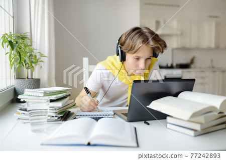 Teenager boy study at home. Online education and distance learning for children. School boy doing his physics homework using gadgets. Lessons on the internet for high school students Teenager boy study at home. Online education and distance learning for children. School boy doing his physics homework using gadgets. Lessons on the internet for high school students 77242893