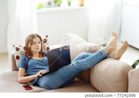 Young woman working with laptop computer lying on sofa at home. Freelancer or blogger. Distance learning of new profession. Additional education. Retraining courses. Business online 77242896