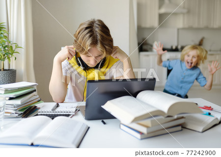 Tennager boy study at home. Online education and distance learning for children. School boy doing his homework using gadgets. Lectures and lessons on the internet for high school students 77242900